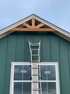 a ladder is attached to the side of a green building with windows and a sky background