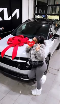 a woman standing next to a white car with a red bow on it