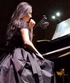 a woman sitting at a piano in front of a microphone