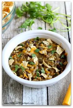 a white bowl filled with chicken and tortilla soup on top of a wooden table