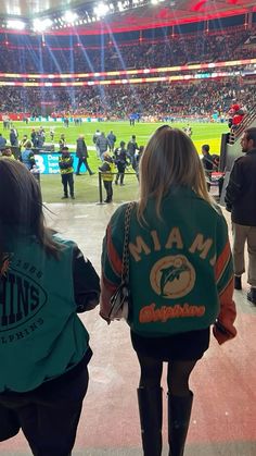 two women in matching jackets are walking towards the stands at a football game with fans