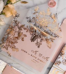 pink and gold wedding stationery with flowers on marble table top next to envelopes