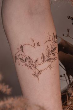 a tattoo on the leg of a woman with leaves and moon in the shape of a heart