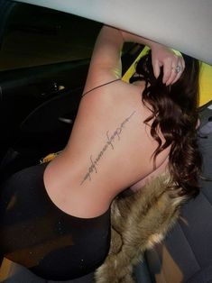 a woman sitting in the back seat of a car with a tattoo on her lower back