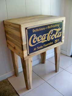 an old coca - cola cooler sitting on top of a wooden stool