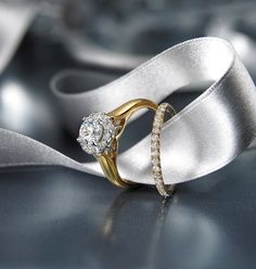 two wedding rings with white satin ribbon on top of each other and one diamond in the middle