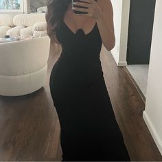 a woman in a black dress taking a selfie with her cell phone while standing in a living room