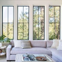 a living room filled with furniture and large windows over looking the trees in the distance