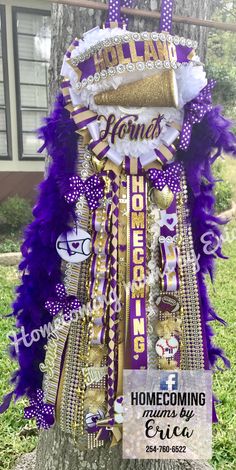 a purple and gold decoration hanging from a tree in front of a house with the words home coming on it