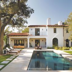 a large white house with a pool in the front yard and lounge chairs around it