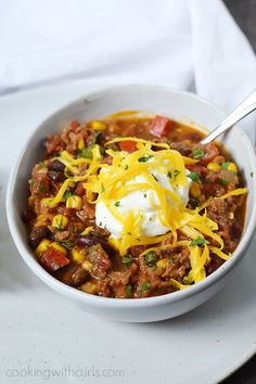 a white bowl filled with chili and sour cream on top of a plate next to a fork