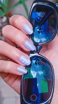 a woman's hand holding two sunglasses with blue and white nail polishes on them