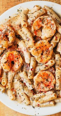 a white plate topped with pasta covered in shrimp and seasoning on top of a wooden table