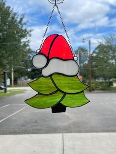 a stained glass christmas ornament hanging from a chain on a parking lot with trees in the background