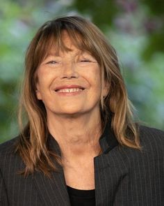 an older woman with long hair smiling at the camera while wearing a black shirt and striped blazer