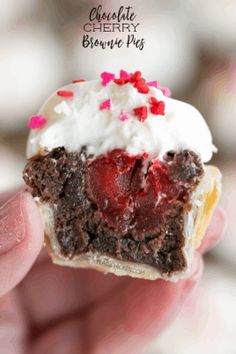 someone holding up a chocolate cherry brownie pie with white frosting and sprinkles