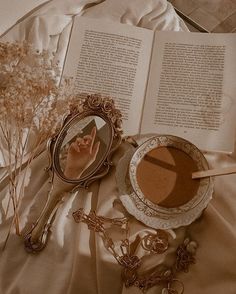 an open book, mirror and flowers on a bed with a cup of coffee next to it