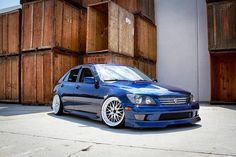 a blue car is parked in front of some wooden walls and fenced in area