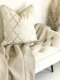 a white couch with two pillows on top of it next to a vase filled with dry grass