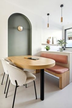 a wooden table sitting under a window next to a white bench with two beige chairs