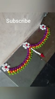 a colorful beaded bracelet on the ground next to a white wall with words subscribe