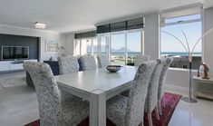 a dining room table with chairs and a bowl of fruit on it in front of large windows overlooking the ocean