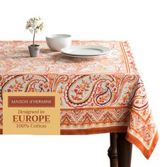 an orange and white table cloth on top of a wooden table with a plate, cup and saucer