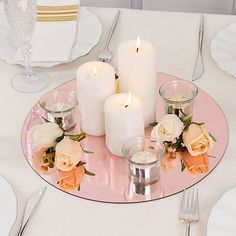 candles are lit on a pink plate with white flowers and roses in the center, along with silverware