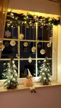 a window with christmas decorations hanging from it's windowsill, and a teddy bear sitting in the window sill