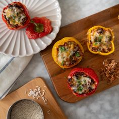 three stuffed peppers sitting on top of a wooden cutting board next to rice and spoons