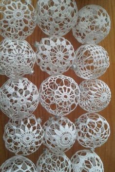 white crochet doily balls are arranged on a wooden surface, ready to be made into decorative ornaments