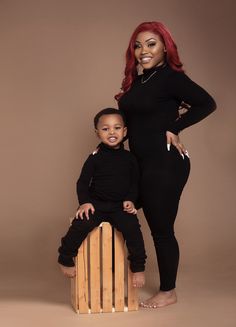 a woman standing next to a child on top of a wooden block in front of a brown background