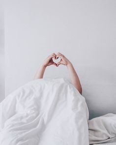 a person laying in bed making a heart shape with their hands