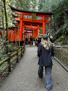 a woman is walking down a path in front of an orange torimi gate with people standing around it