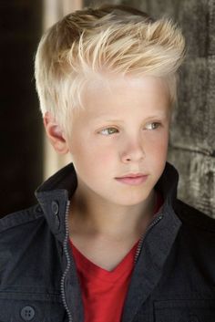 a young boy with blonde hair wearing a black jacket and red shirt looking at the camera