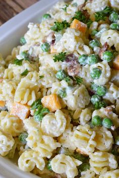 pasta salad with peas and carrots in a white bowl on a wooden table top