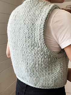 a woman is wearing a knitted sweater vest over her shoulder and looking in the mirror