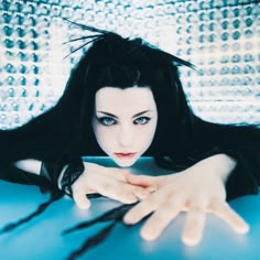 a woman with long black hair sitting on top of a blue table holding her hands out