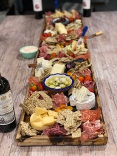 a wooden table topped with lots of different types of cheese and meats next to bottles of wine