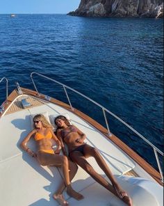 two women in bikinis lounging on the back of a boat near an island