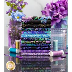 there are many different types of fabrics on the table with purple flowers in the background