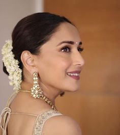 a woman in a white dress with flowers in her hair and wearing an elaborate necklace