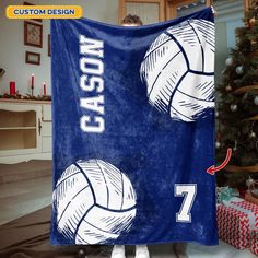 a woman is holding up a blue towel with volleyballs on it in front of a christmas tree