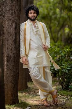 a man standing next to a tree wearing a white suit and tie with gold trims