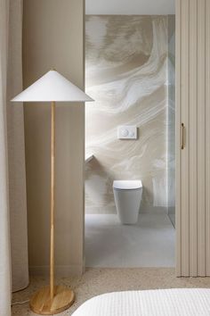 a white toilet sitting next to a wooden floor lamp in a room with beige walls