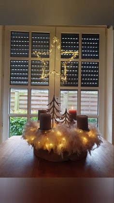 a wooden table topped with two candles and a basket filled with white feathers on top of it