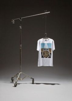 a t - shirt hanging on a clothes rack next to a tripod with an image of a beach