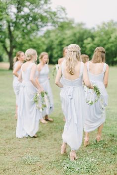 bridesmaids in white dresses walking through the grass together with their backs to the camera