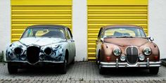 two old cars parked next to each other in front of yellow garage doors with graffiti on them