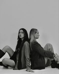 two women are sitting on the floor and one is looking off to the side with her legs crossed